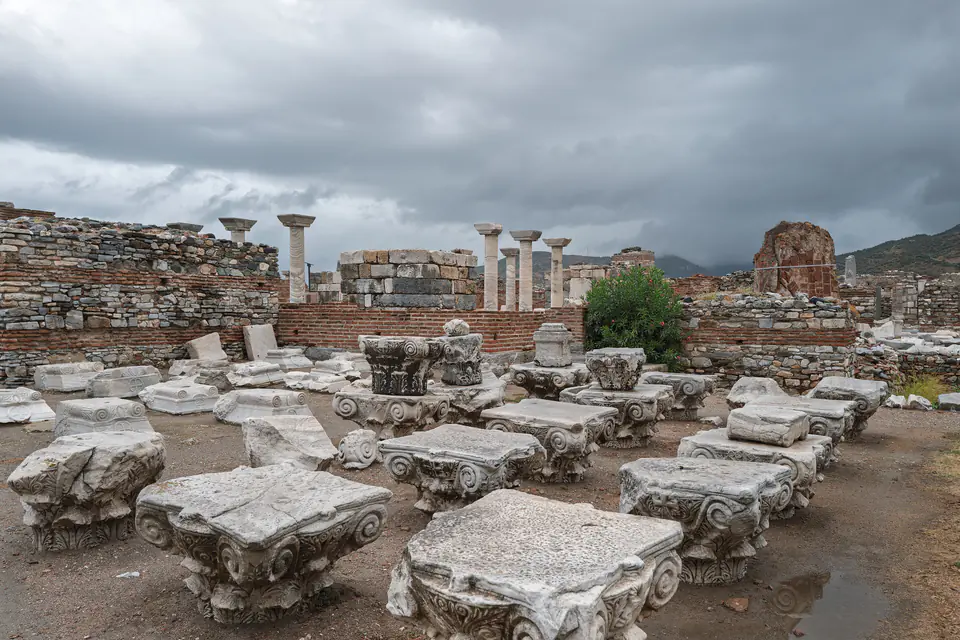 Rows of carved capitals laid out in the nave of the Basilica of St John under a stormy sky