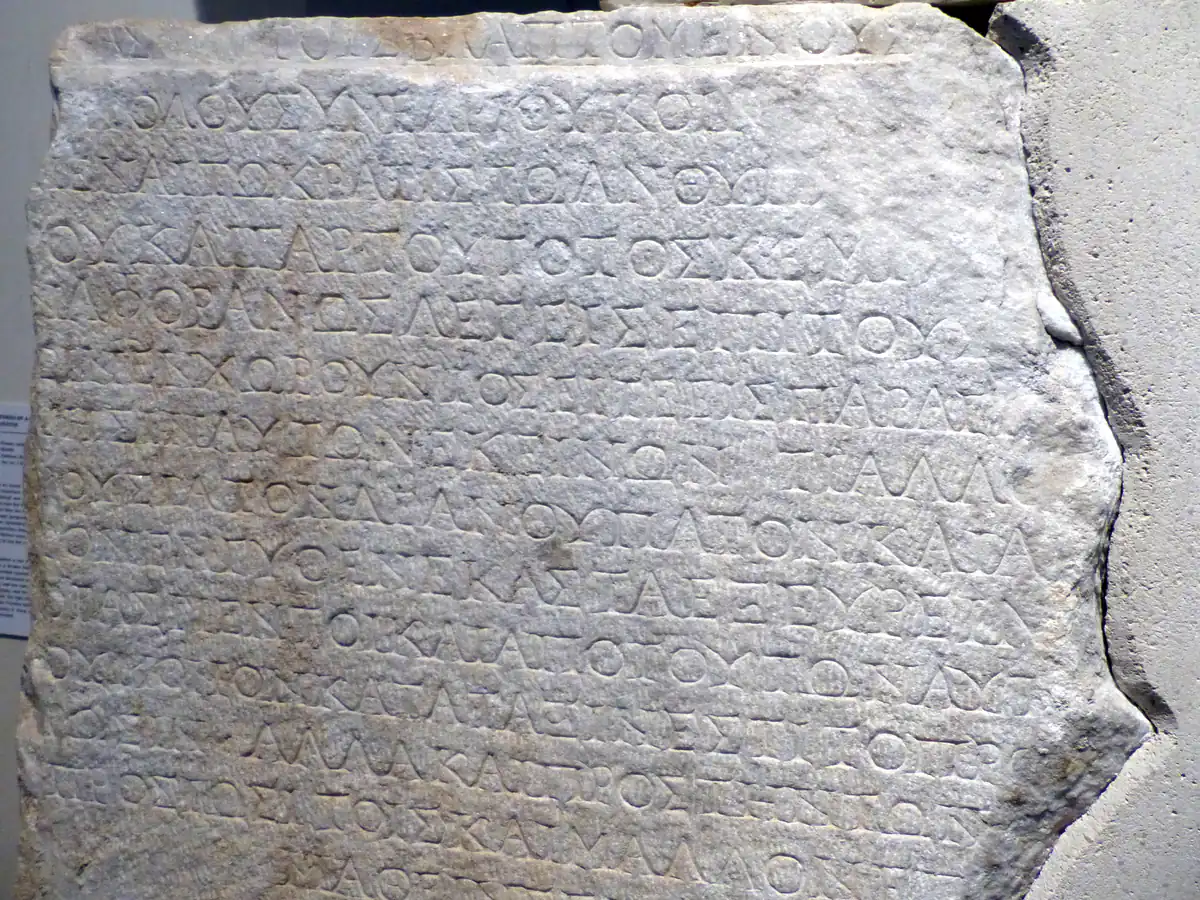 Closely spaced Greek lettering carved into a pale marble slab in a museum display