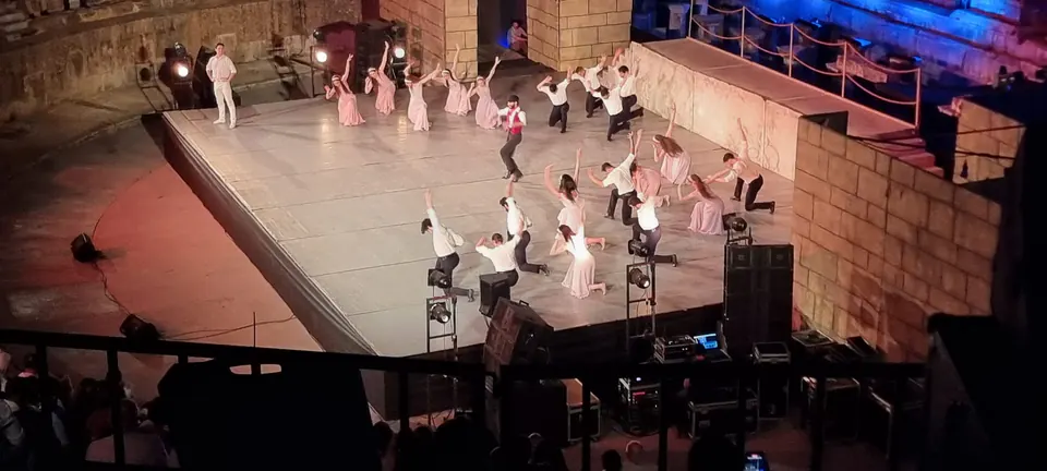 Efes Büyük Tiyatro'daki sahnede düzen almış topluluk: açık renk elbiseli kadınlar, beyaz gömlekli erkekler, 2026'daki Zorba balesinden.