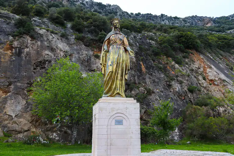 Gilded statue of the Virgin Mary on a pedestal against the rocky hillside at Meryemana