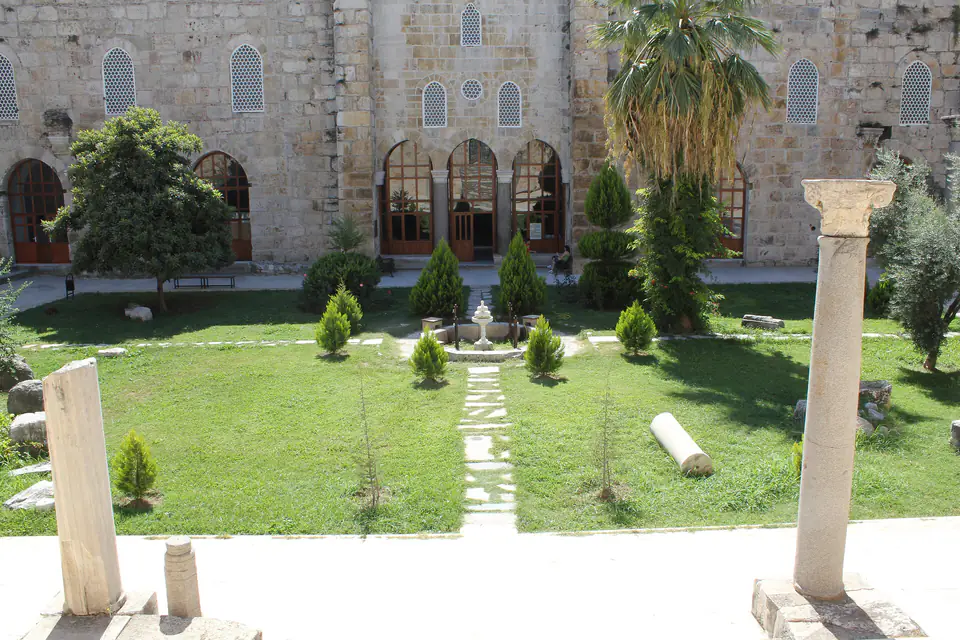 The garden courtyard of the İsa Bey Mosque, with an arcade, a palm and a column