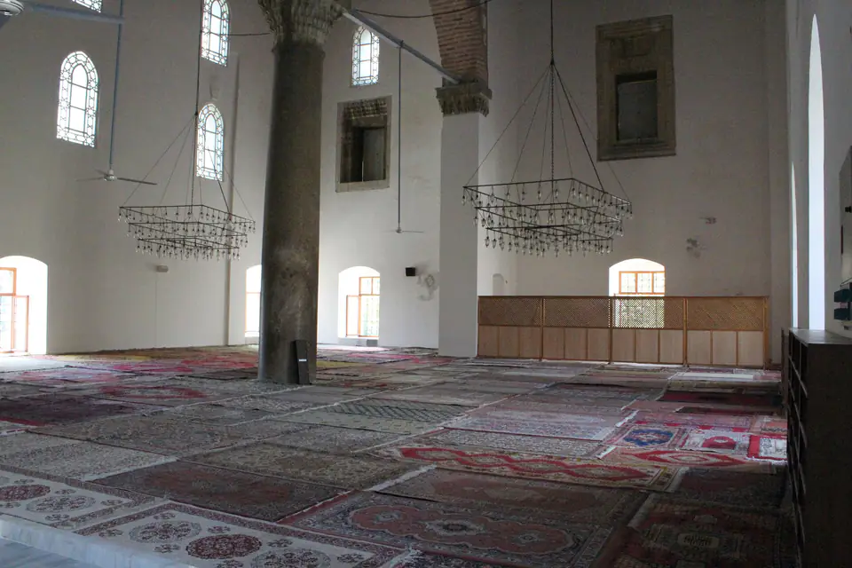The prayer hall of the İsa Bey Mosque, with carpets, a column and hanging lamps