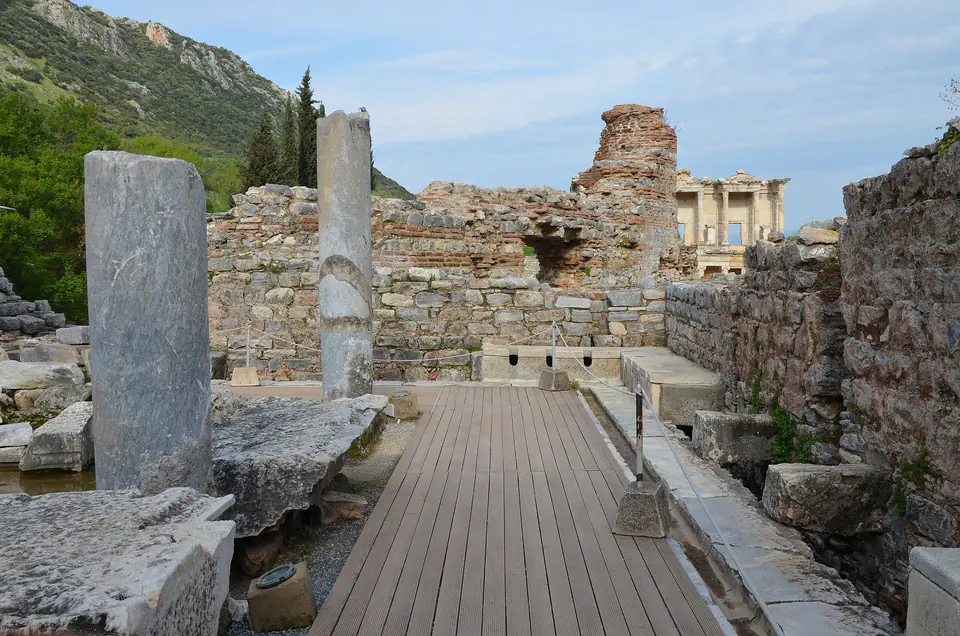Le latrine pubbliche di Efeso, con una passerella in legno e la biblioteca di Celso visibile in lontananza