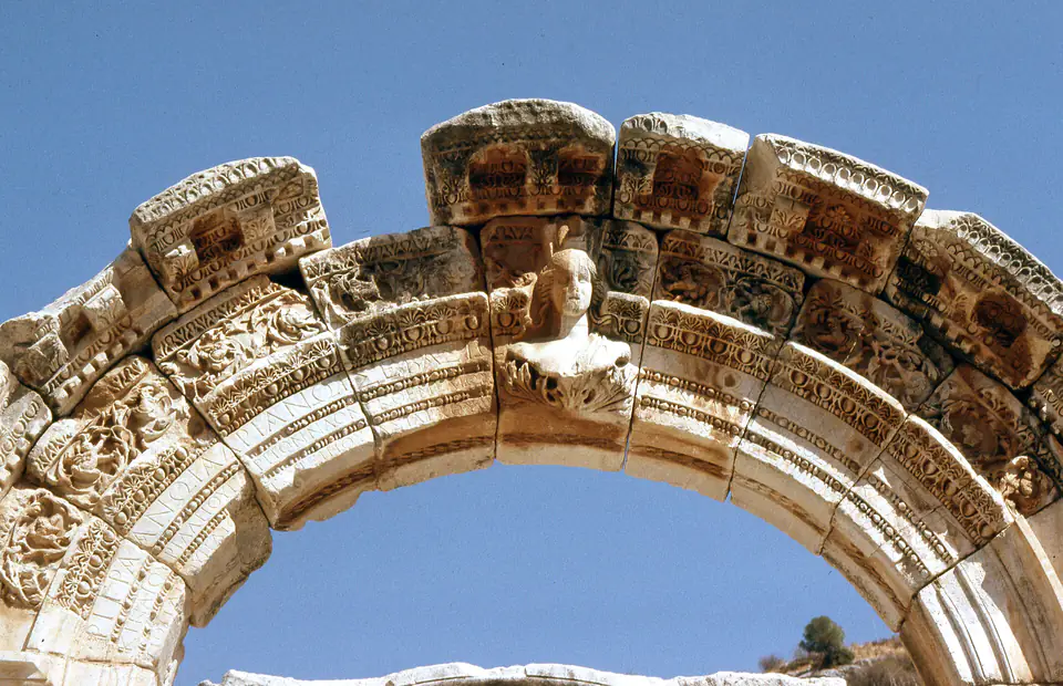 The carved arch of the Temple of Hadrian with a bust at its centre against a blue sky